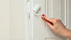 Hand streicht mit einer kleinen Farbrolle weiß über eine Türrahmenkante