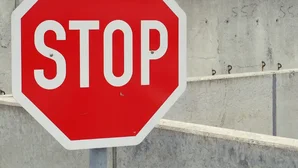 Rotes Stoppschild mit der Aufschrift 'STOP' vor einer grauen Wand.