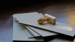 Holzstempel liegt auf mehreren verschlossenen Briefumschlägen auf einem dunklen Tisch