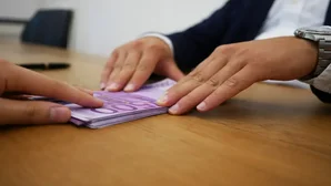 Zwei Personen tauschen Geldscheine in 500-Euro-Noten über einen Holztisch aus