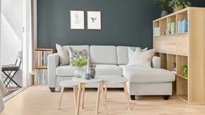Modern eingerichtetes Wohnzimmer mit grauem Sofa, Holzregal, runden Tischen und dunkelgrüner Wand